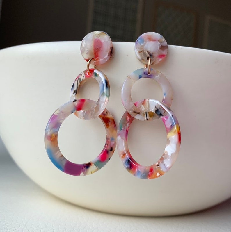 May include: A pair of colorful, multi-colored, multi-patterned, acrylic, dangle earrings with three linked circles. The circles are in a graduated size, with the largest circle at the bottom.