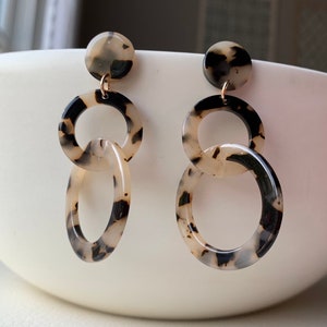 May include: A pair of dangle earrings with a tortoiseshell pattern. The earrings feature three linked circles, with the top circle being the smallest and the bottom circle being the largest.