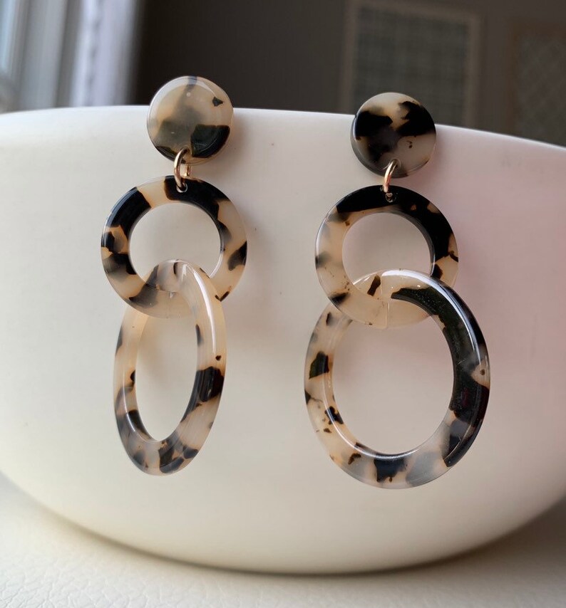 May include: A pair of dangle earrings with a tortoiseshell pattern. The earrings feature three linked circles, with the top circle being the smallest and the bottom circle being the largest.