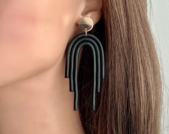 May include: A dangle earring featuring a circular gold-tone stud connected to a black arch-shaped pendant. The pendant consists of three nested, U-shaped segments of varying lengths, creating a layered, tiered appearance that hangs vertically.