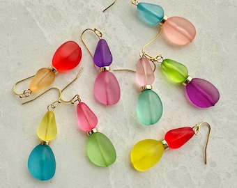 May include: A set of six pairs of dangle earrings with two teardrop-shaped beads on each earring. The beads are in various colors, including pink, purple, green, blue, yellow, and red.