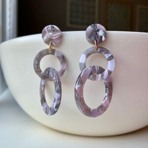 May include: A pair of dangle earrings with a gray and pink marbled pattern. The earrings feature three circles, with the top circle being the smallest and the bottom circle being the largest.
