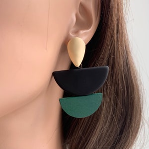 May include: A pair of statement earrings with a teardrop-shaped top piece in cream, a black half-circle, and a green half-circle.