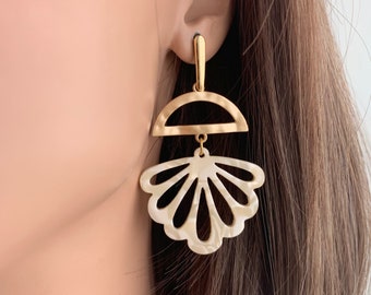 May include: Gold tone earrings with a white shell-shaped design. The shell has a cutout pattern and is suspended from a gold arch.