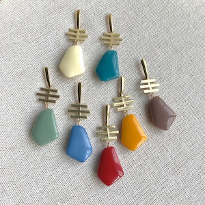 May include: Set of 7 gold earrings with colorful geometric stone pendants. The stones are in shades of blue, green, yellow, red, and brown.