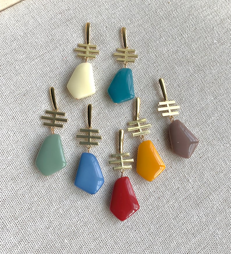May include: Set of 7 gold earrings with colorful geometric stone pendants. The stones are in shades of blue, green, yellow, red, and brown.