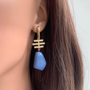 May include: Gold geometric dangle earrings with a light blue stone pendant.