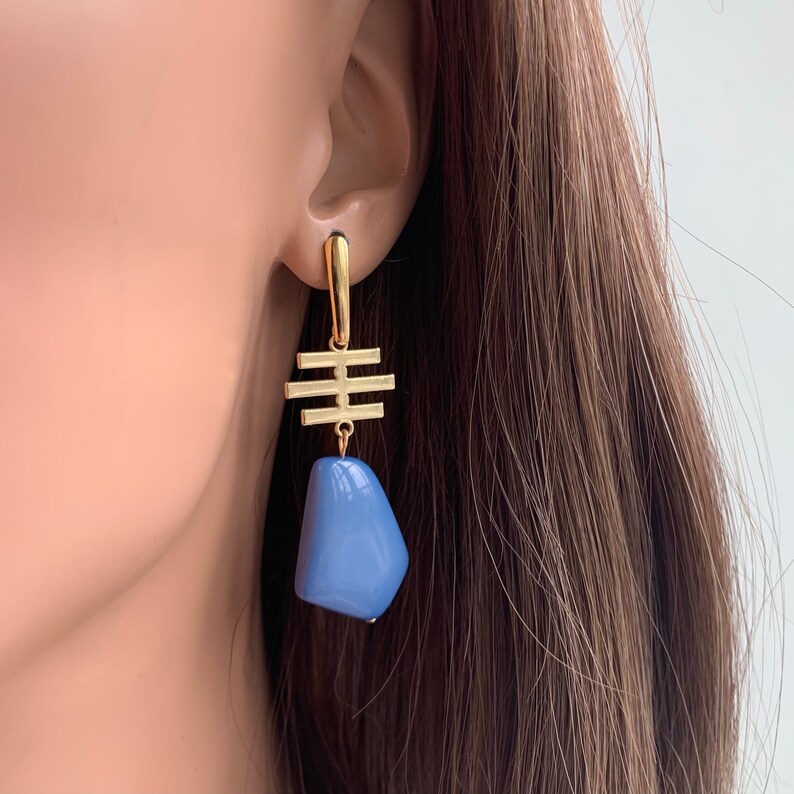May include: Gold geometric dangle earrings with a light blue stone pendant.