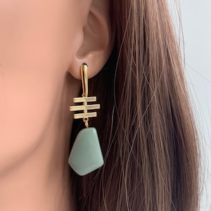 May include: Gold dangle earrings with a geometric design and a light green stone pendant.