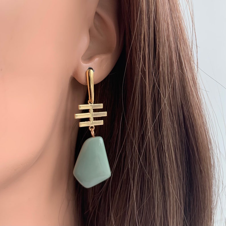 May include: Gold dangle earrings with a geometric design and a light green stone pendant.