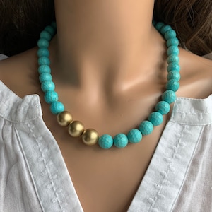 May include: A turquoise and gold beaded necklace. The necklace is made of round turquoise beads with a gold accent in the center.