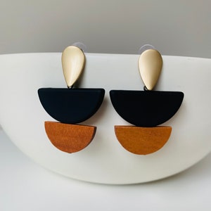 May include: A pair of geometric earrings with a gold teardrop top, a black half-circle, and a brown half-circle.
