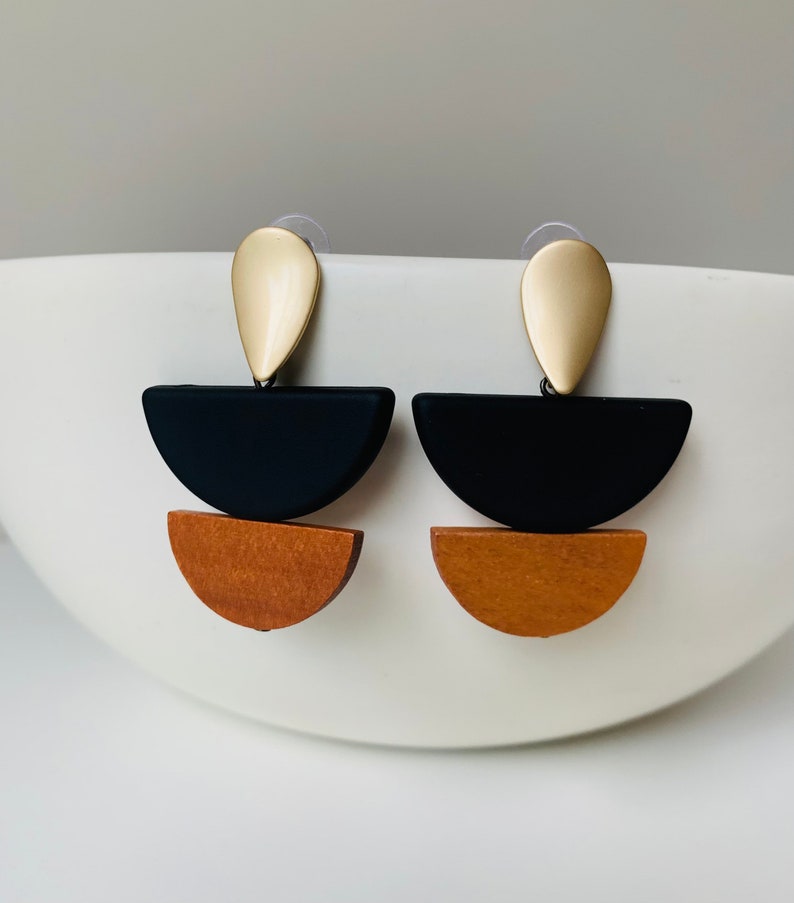 May include: A pair of geometric earrings with a gold teardrop top, a black half-circle, and a brown half-circle.