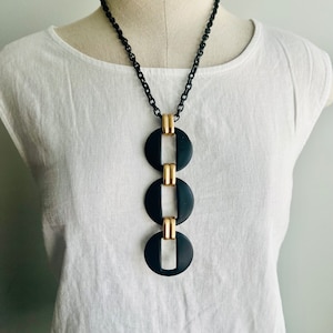May include: A black and gold necklace with a geometric design. The necklace features three large, black, circular pendants with gold accents. The pendants are connected by a black chain.