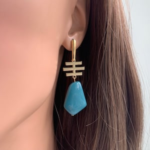 May include: Gold geometric dangle earrings with a teal blue stone pendant.