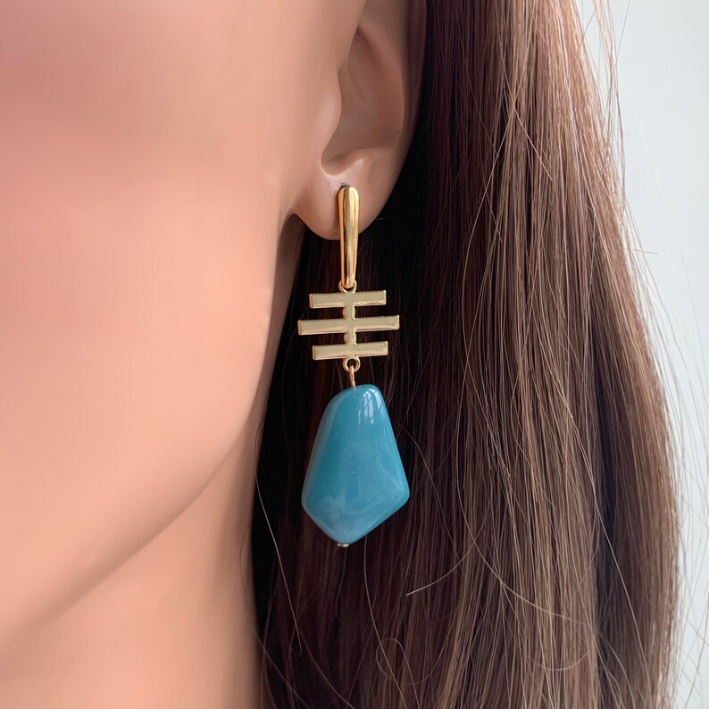 May include: Gold geometric dangle earrings with a teal blue stone pendant.