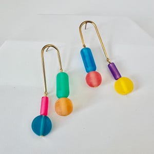 May include: A pair of gold hoop earrings with colorful glass beads. The earrings feature a blue, green, pink, and yellow bead on each hoop.