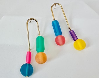 May include: A pair of gold hoop earrings with colorful glass beads. The earrings feature a blue, green, pink, and yellow bead on each hoop.