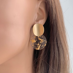 May include: Gold and clear resin earrings with gold flakes. The earrings are a circle shape and are layered on top of each other.