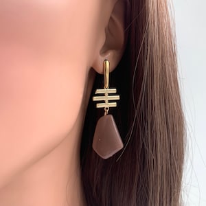 May include: Gold geometric earrings with a brown stone pendant. The earrings have a simple, modern design.