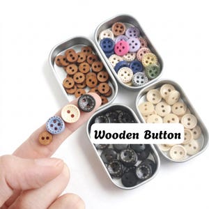 Könnte beinhalten: Eine Sammlung kleiner runder Holzknöpfe in verschiedenen Farben wie Braun, Schwarz, Weiß, Blau, Pink und Grün, sortiert in drei rechteckigen Metalldosen. Der Text "Wooden Button" ist in Schwarz auf einem weißen rechteckigen Etikett aufgedruckt.