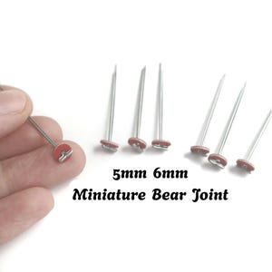 May include: A set of silver-toned metal pins with small red circular discs at the base, labelled 5mm 6mm Miniature Bear Joint. These metal fasteners feature a long, thin shaft and a T-shaped connector on the flat red disc, designed for crafting.