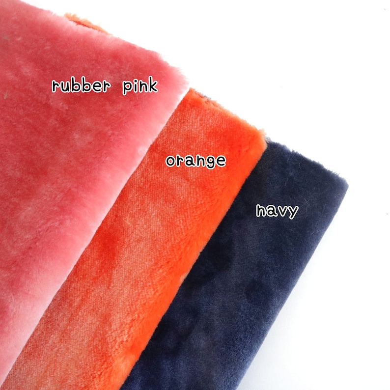 May include: Three fabric swatches in different colors: rubber pink, orange, and navy. The swatches are folded over each other, with the pink swatch on top.