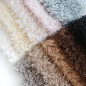 Puede incluir: Primer plano de una colección de muestras de tela de piel sintética en varios colores. Los colores incluyen crema, rosa, gris, marrón y negro. La tela tiene un aspecto rizado y texturizado.