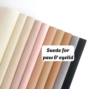 May include: A collection of suede fabric sheets arranged in a fan pattern, featuring a gradient of neutral colors ranging from cream and beige to soft pink, tan, brown, gray, and black. The text "Suede for paw & eyelid" is printed on the image.