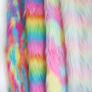 Può includere: Quattro strisce verticali di tessuto in pelliccia sintetica a pelo lungo disposte fianco a fianco. La prima striscia presenta vivaci colori arcobaleno, la seconda mostra un brillante gradiente multicolore, la terza tonalità arcobaleno pastello e la quarta una delicata miscela pastello.