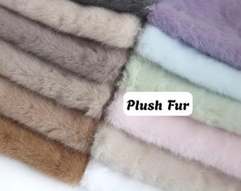 May include: A collection of plush faux fur fabric swatches arranged in a layered stack. The colors include white, tan, brown, gray, lavender, light blue, mint green, and pale pink. A white rectangular label displays the text Plush Fur.
