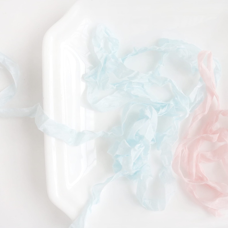 May include: A close-up of two spools of ribbon, one light blue and one pale pink, on a white surface.