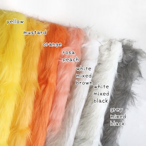 Op de afbeelding: Een collectie kunstbont stofstalen gerangschikt in een rij, met kleuren gelabeld als geel, mosterd, oranje, roze perzik, wit gemengd bruin, wit gemengd zwart en grijs gemengd zwart, met lange, zachte en getextureerde vezels.