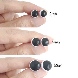 Op de afbeelding: Drie paar ronde, zwart-witte plastic veiligheidsogen voor knutselwerk, getoond in de maten 8mm, 9mm en 12mm. Elk paar heeft een effen zwarte pupil gecentreerd op een witte basis, gepresenteerd in een helder overzicht voor maatvergelijking.