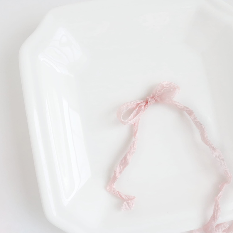 May include: A pink ribbon tied in a bow on a white ceramic plate.
