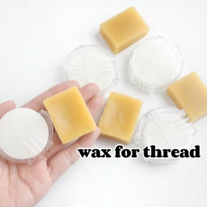 May include: Six small bars of yellow wax for thread, in clear plastic containers. The text "wax for thread" is printed below the bars of wax.