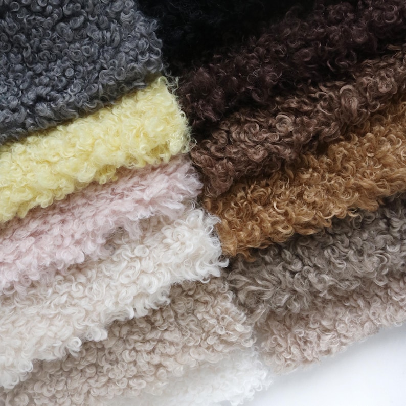 May include: A collection of curly faux fur fabric swatches arranged in a layered stack. The colors include shades of charcoal gray, pale yellow, soft pink, cream, white, dark brown, tan, and light taupe, all featuring a dense, textured pile.