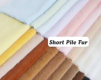Puede incluir: Una colección de muestras de tela de piel de pelo corto dobladas en una variedad de colores que incluyen azul claro, amarillo, blanco, rosa, beige, naranja, marrón y negro. Se ve una etiqueta rectangular blanca con el texto negro Short Pile Fur.