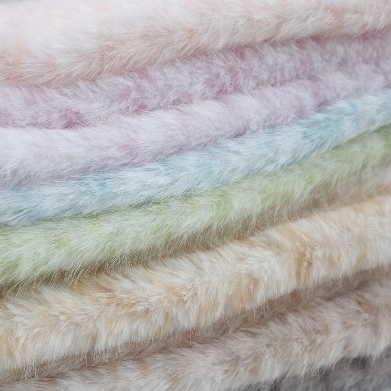May include: Close-up of a stack of faux fur fabric in various pastel colors. The colors include pink, lavender, light blue, green, beige, and gray. The fur appears soft and fluffy, with a slight sheen.
