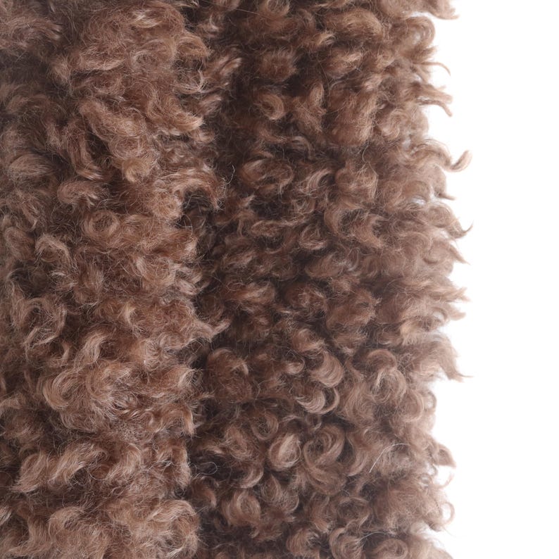 May include: Close-up of a brown, curly fur texture. The fur has a dense, wavy pattern with varying shades of brown, creating a soft and inviting appearance. The texture is detailed and appears to be a natural material.