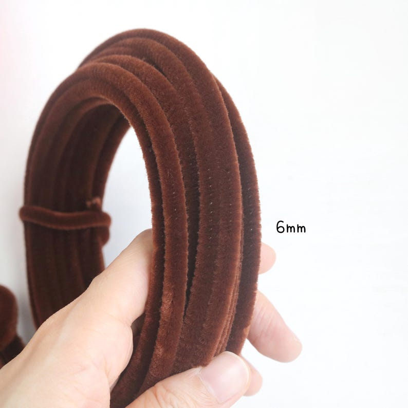 May include: A coiled length of dark brown velvet piping trim with a soft, fuzzy texture. The trim features a consistent cylindrical shape and is labeled with the text 6mm, indicating its diameter for use in various sewing and craft projects.