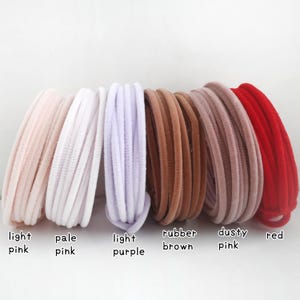 May include: A collection of six coiled hair ties in various colors, labeled as light pink, pale pink, light purple, rubber brown, dusty pink, and red. Each hair tie features a soft, velvet-like texture and a rounded, flexible cord design.