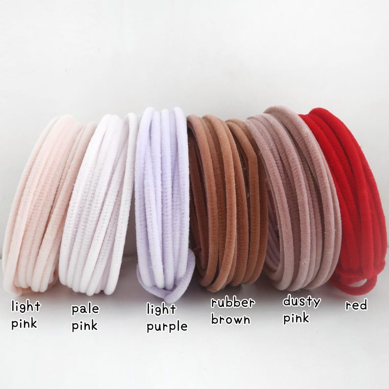 May include: A collection of six coiled hair ties in various colors, labeled as light pink, pale pink, light purple, rubber brown, dusty pink, and red. Each hair tie features a soft, velvet-like texture and a rounded, flexible cord design.