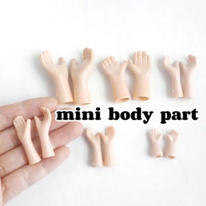 May include: A collection of small, tan-colored plastic hands, some open and some closed, arranged on a white surface. The text "mini body part" is displayed in black letters.