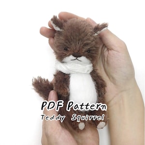 May include: A small, plush, brown and white squirrel toy with a fuzzy texture, pointed ears, and a white scarf around its neck. The text 'PDF Pattern Teddy Squirrel' is printed in black letters over the center of the squirrel's body.
