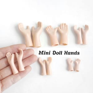 May include: A collection of light-toned plastic doll hands in various sizes and poses, arranged in pairs. The set includes several distinct styles of miniature hands, some held in an open palm position and others with fingers curled. Text reads Mini Doll Hands.