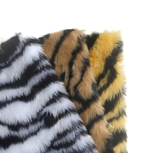 May include: Three swatches of faux fur fabric featuring animal-inspired patterns. The first swatch has a white and black zebra stripe design, the second has a tan and black tiger stripe pattern, and the third has a yellow and black tiger stripe pattern.