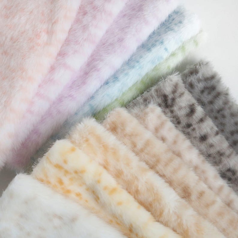 May include: A collection of faux fur fabric samples in various pastel colors. The samples include shades of pink, lavender, blue, green, beige, and gray, each with a spotted pattern. The fur has a soft, fluffy texture.