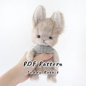 Pode incluir: Um coelho de pelúcia bege com orelhas compridas, olhos escuros e um nariz pequeno, usando um lenço de pescoço xadrez cinza e branco. A imagem inclui o texto PDF Pattern Teddy Rabbit sobreposto ao brinquedo de pelúcia em uma fonte preta clara.