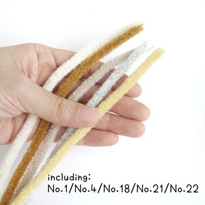 May include: Five different colored chenille stems, including No. 1, No. 4, No. 18, No. 21, and No. 22. The stems are held in a hand.